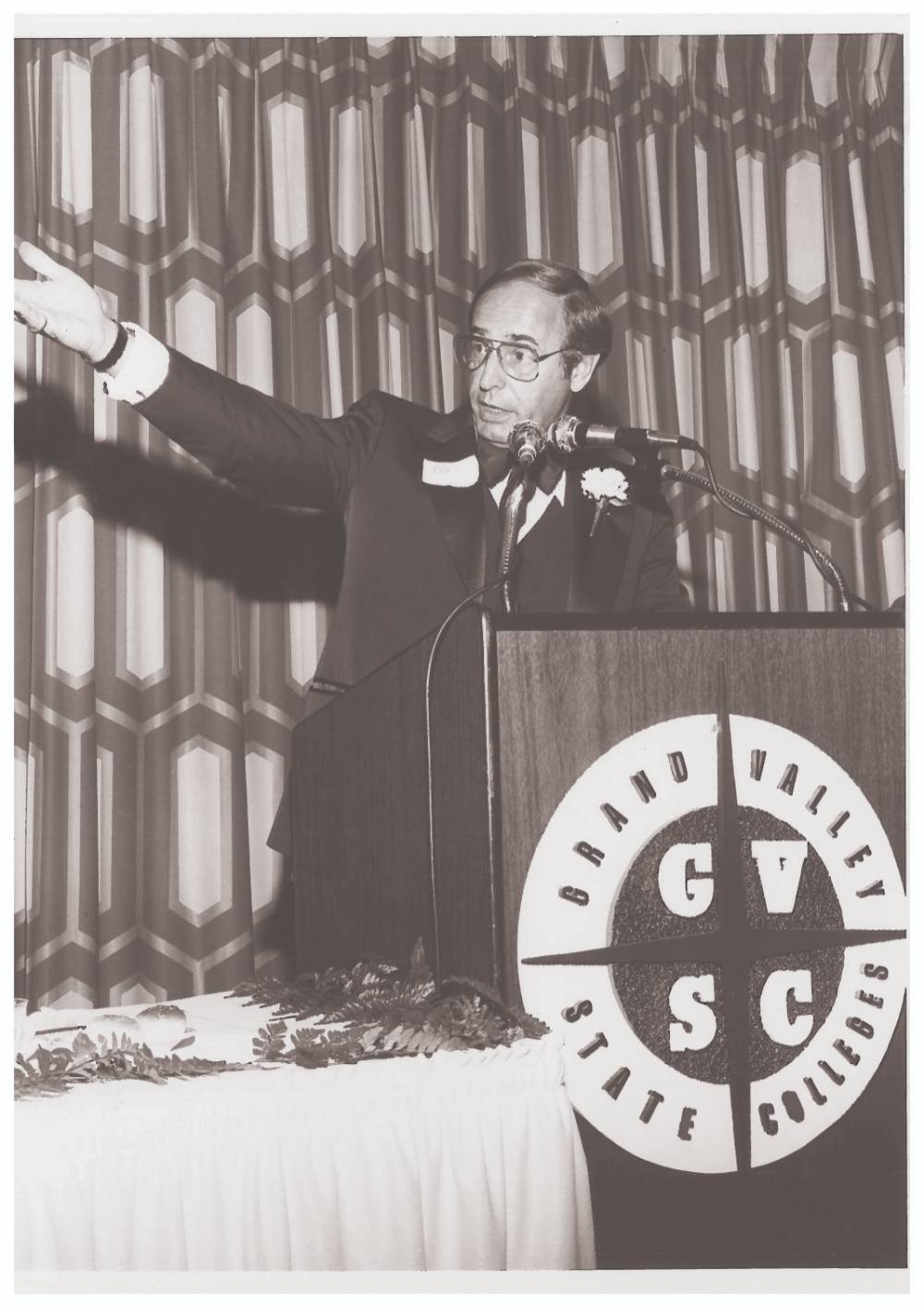 Richard DeVos standing at a podium speaking with his arm extended.